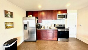 A compact kitchen with wooden cabinets, stainless steel appliances, and a tiled backsplash. - 2b-1b nearby beach (Daly City)