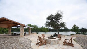 Eine Terrasse im Freien mit Steinböden, Holzstühlen, einer Feuerstelle und einem überdachten Sitzbereich mit Blick auf einen See.