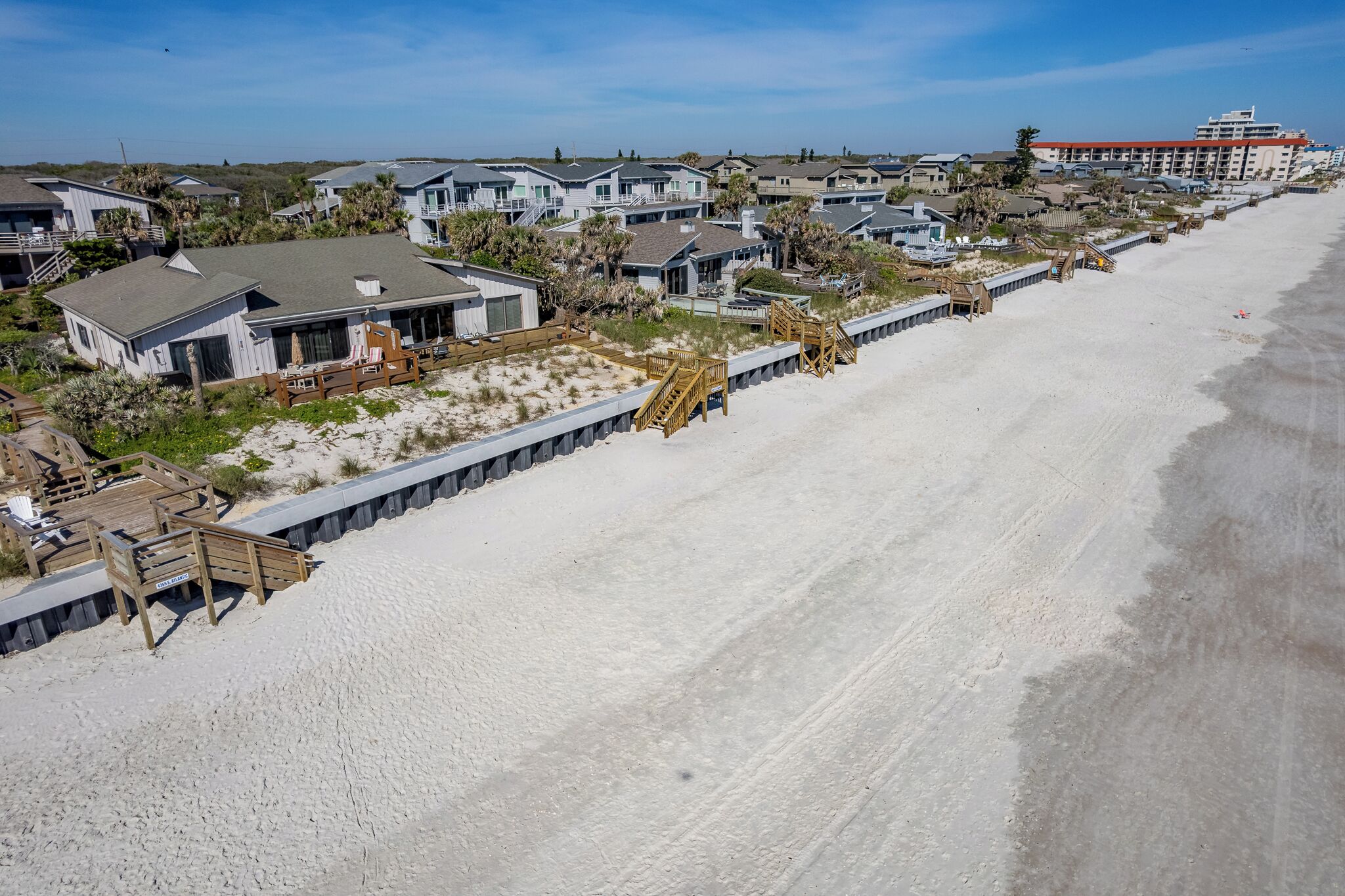 A beachfront property with multiple houses, a wooden boardwalk, and a sandy beach.