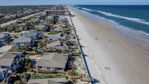An aerial view of a coastal residential area with beachfront properties, a boardwalk, and a large hotel with multiple floors.