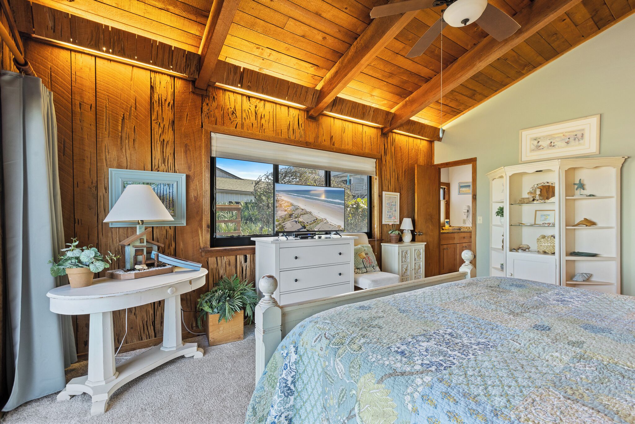 A bedroom with a large bed, wooden walls, a window with a view, a dresser, and a vanity.