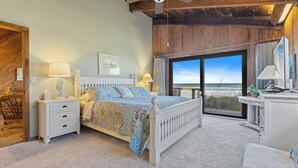 A bedroom with a large bed, a desk, and a view of the beach.