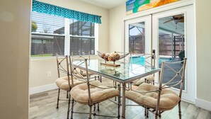 A dining area with a glass table and cushioned chairs, a view of a swimming pool, and a painting above the door.
