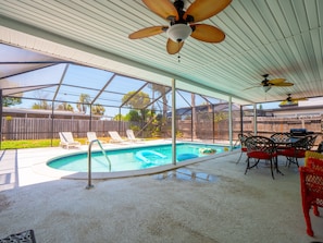 A covered outdoor swimming pool area with lounge chairs and a dining table.