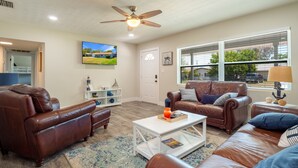 A living room with leather sofas, a coffee table, a TV, and a ceiling fan.