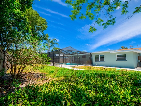 A modern house with a glass-enclosed patio, surrounded by lush greenery and a clear blue sky.