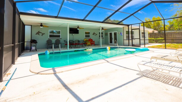 A covered outdoor swimming pool with a patio area, including seating and a ceiling fan.