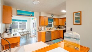 A compact kitchen with wooden cabinets, a dining area with a table and chairs, and a view of the outdoors through a window.