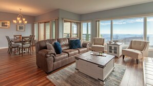 A spacious living room with a brown leather sofa, a coffee table, and a view of the mountains through large windows. - WINTERGREEN RESORT HOME WITH BLUE RIDGE VIEWS (Wintergreen Resort)
