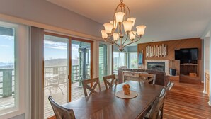 A spacious dining area with a wooden table and chairs, a chandelier, and large windows offering a view of a deck and mountains. - WINTERGREEN RESORT HOME WITH BLUE RIDGE VIEWS (Wintergreen Resort)