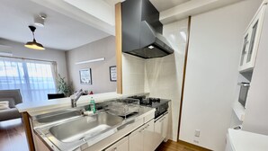 A modern kitchen with a central island, stainless steel appliances, and a black range hood. - Luana Lea Karate Kaikan Mae (Tomigusuku)