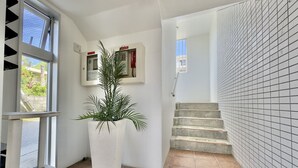 A hallway with a potted plant, a staircase, and tiled walls. - Luana Lea Karate Kaikan Mae (Tomigusuku)