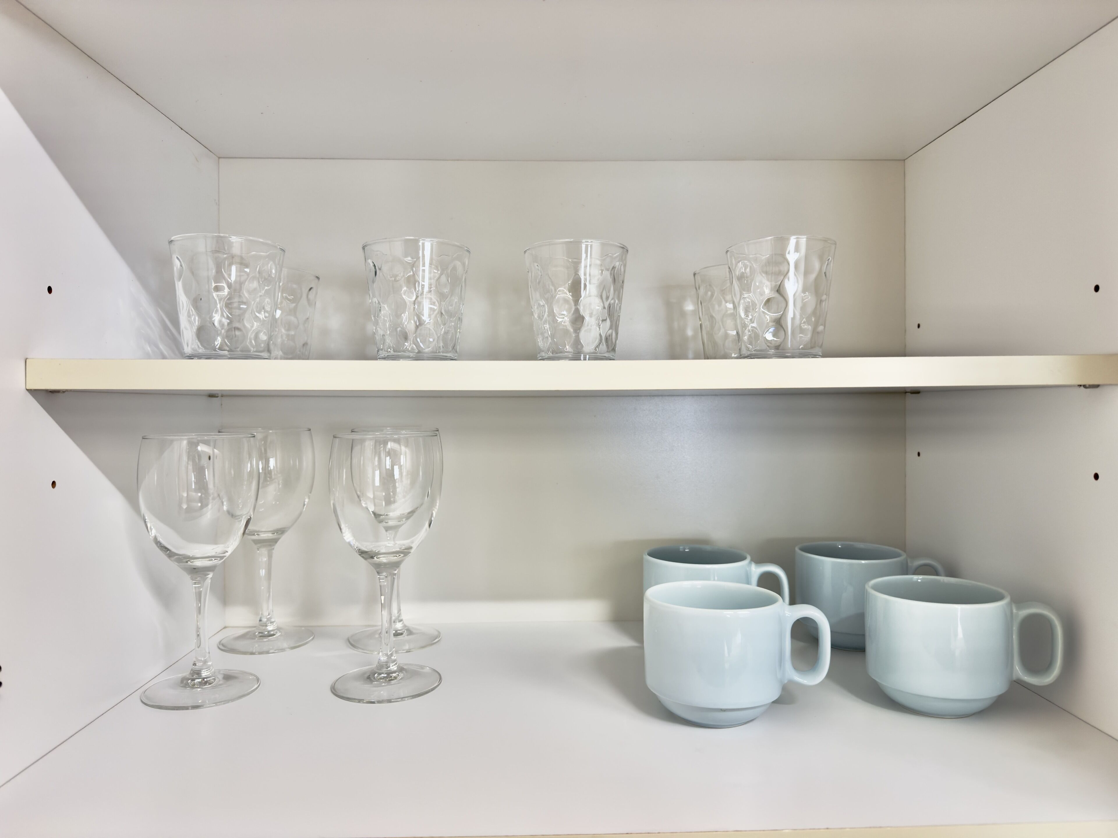 A shelf with clear glassware and white ceramic mugs.