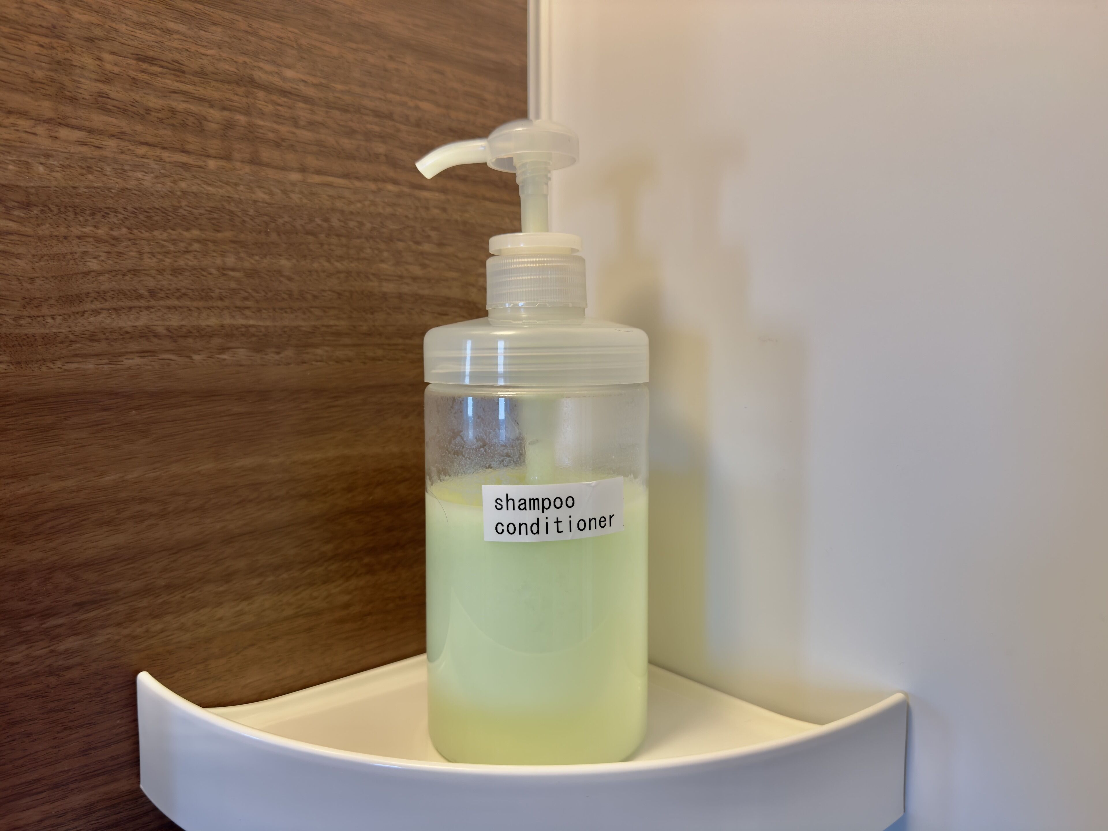 A bathroom with a white shelf holding a clear bottle of shampoo conditioner.