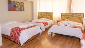 Habitación de hotel con tres camas, cada una con colcha blanca y detalles rojos, y un cuadro abstracto colorido en la pared.