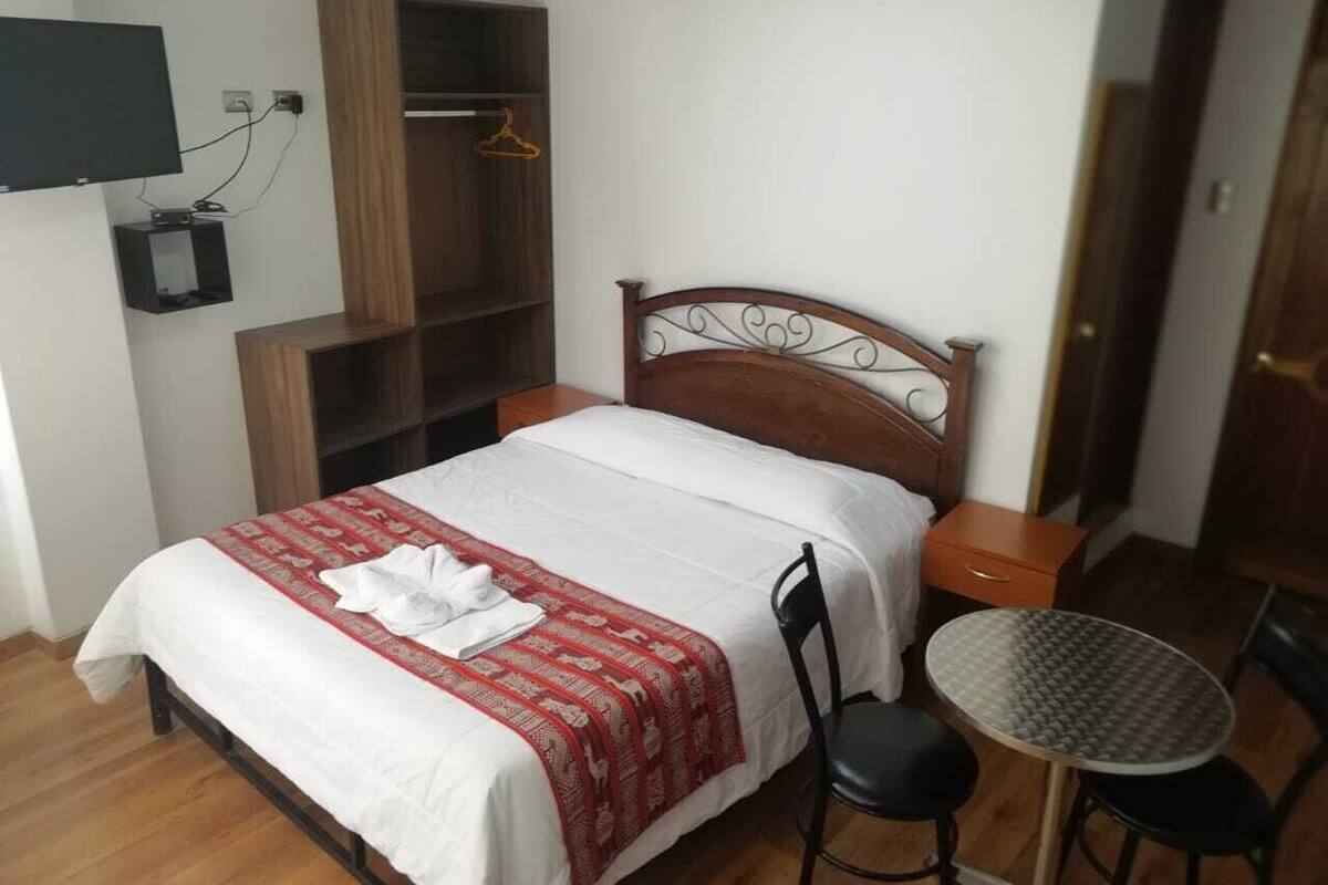 Une chambre bien rangée, avec un lit, une table de chevet, une chaise et une petite table ronde.
