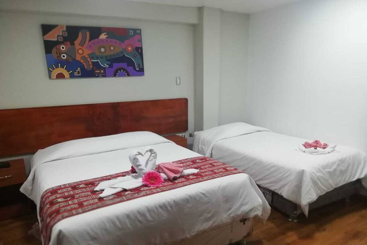 Une chambre d’hôtel avec deux lits, chacun recouvert d’une literie blanche et d’une couverture à motifs rouges. Un tableau coloré est accroché au mur, au-dessus des lits.