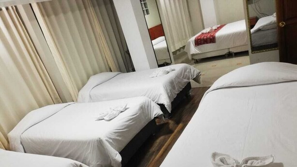 Habitación de hotel con dos camas individuales, cada una con una toalla doblada con cuidado. El piso es de madera y hay un espejo grande en una pared.