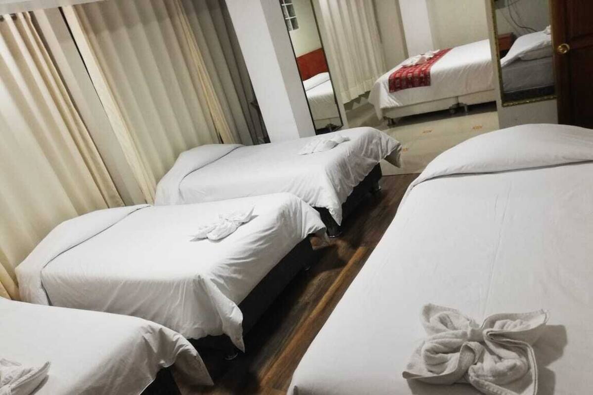 Une chambre d’hôtel avec deux lits simples, chacun agrémenté d’une serviette soigneusement pliée. La chambre est dotée d’un plancher en bois et d’un grand miroir sur l’un des murs.
