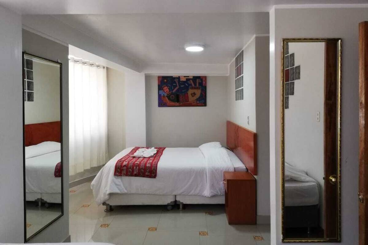Une chambre d’hôtel avec deux lits, une tête de lit en bois, un miroir, un tableau accroché au mur et une porte.