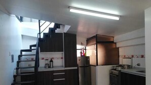 Una cocina con estufa empotrada, refrigerador y pileta. Una escalera conduce a un nivel superior.