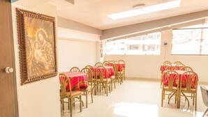Comedor con mesas dispuestas para seis comensales, cada una con mantel rojo y sillas doradas. En la pared, un cuadro religioso enmarco.