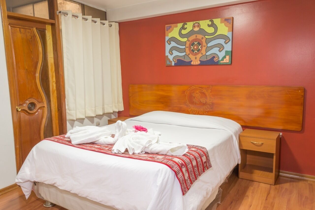 A hotel room with a wooden headboard, a bed with white bedding, a small wooden nightstand, and a colorful abstract painting on the wall.