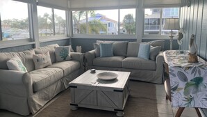 A sunroom with a beige sectional sofa, a small coffee table, and a table with a floral tablecloth. - Dolphins, Sunsets & Waterfront Living – Heated Pool + Dock & Kayaks Near Beaches (Englewood)