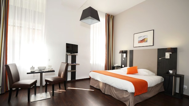 A hotel room with a bed, a desk, a chair, a television, and a window with curtains. - Studio à 10 min du métro | Wifi & gym (Toulouse)