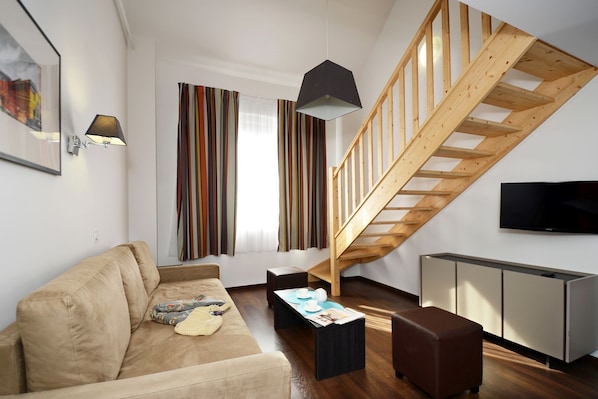 Un salon moderne avec un escalier en bois, un canapé, une table basse et un téléviseur fixé au mur.