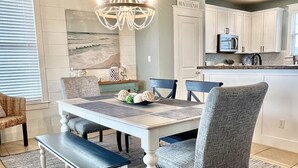 Un espace repas avec une table blanche, des bancs bleus et un lustre.