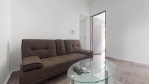 Ein Wohnzimmer mit einem braunen Sofa, einem Glastisch und einer Fernbedienung.