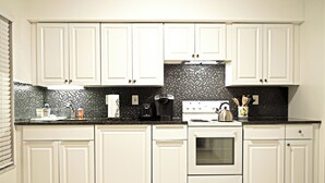 A kitchen with white cabinets, a black tiled backsplash, and a stove. - Home in North Port, AC, Wi-Fi, five minutes walk to Warm Mineral Springs  (North Port)