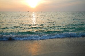 Ein Strand mit Wellen bei Sonnenuntergang, Boote in der Ferne und einem klaren Himmel.