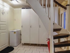 Een trap die naar een tweede verdieping leidt, een witte garderobe, een kleine koelkast en een brandblusser.