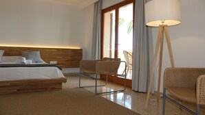 Habitación de hotel con una cama, dos sillas de mimbre, una lámpara de pie y vistas al exterior.