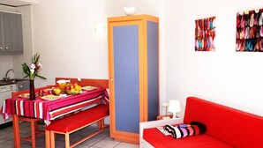 Ein gemütlicher Raum mit Esstisch für zwei Personen, einem roten Sofa, einem hohen Schrank und einer Wand mit farbenfroher Kunst.