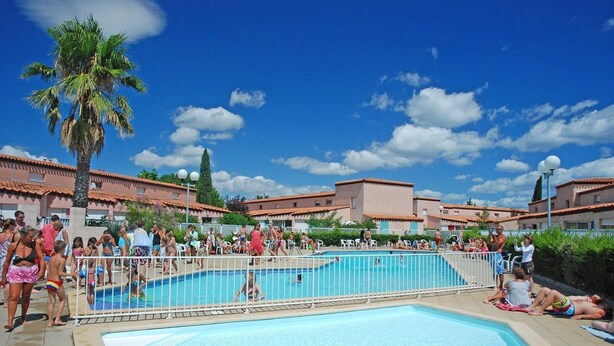Ein Poolbereich mit blauem Himmel, Palmen und Gebäuden mit roten Ziegeldächern.