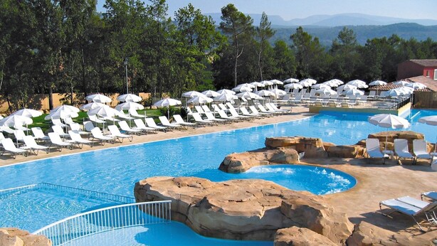 A pool with white lounge chairs and umbrellas, surrounded by rocks and trees. - Maison Équipée + Climatisée | Accès piscine et spa (Fayence)