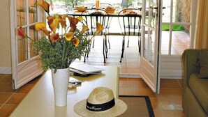 An open door leading to a dining area with a table set for two, a vase with flowers, and a hat on the table. - Maison Équipée + Climatisée | Accès piscine et spa (Fayence)