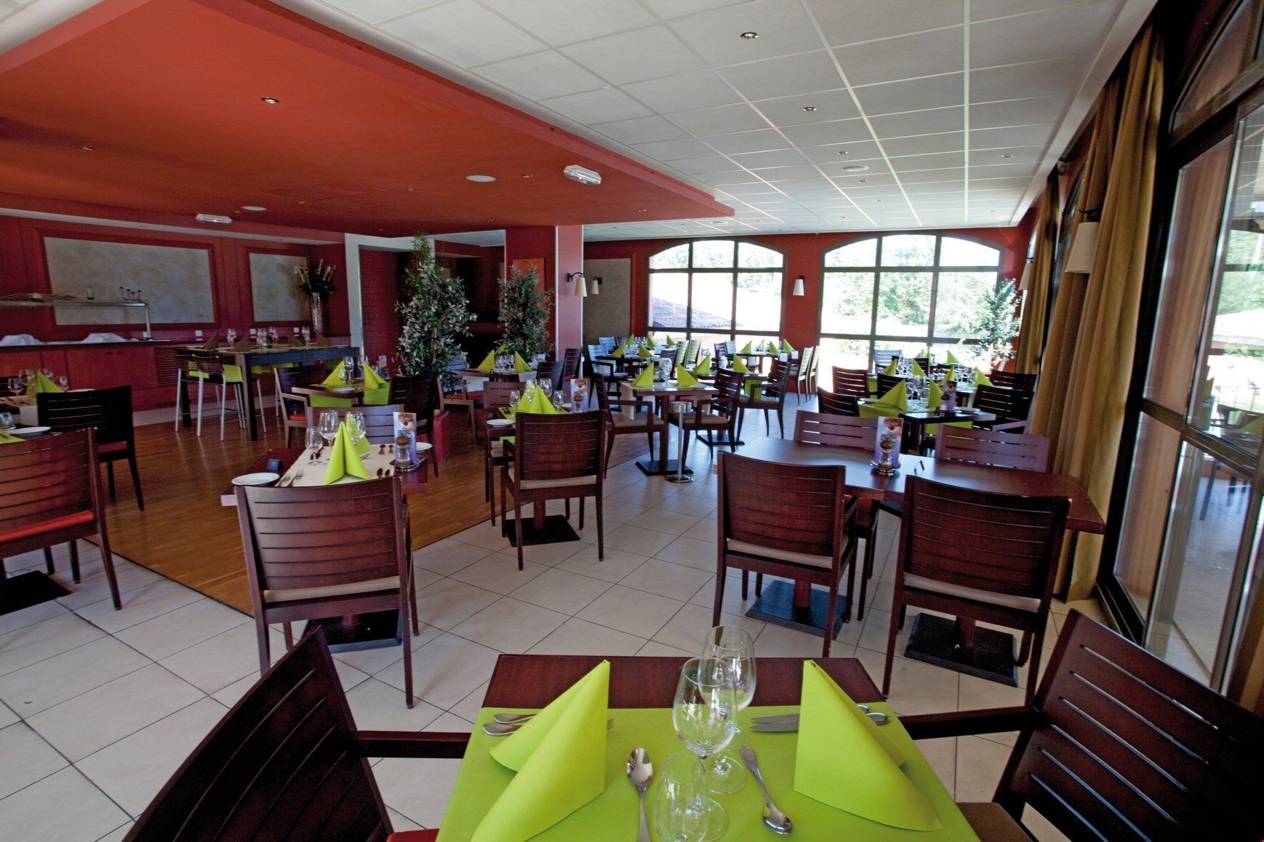 Un restaurant spacieux, doté de nombreuses tables et chaises, de grandes fenêtres et d’un plafond rouge.