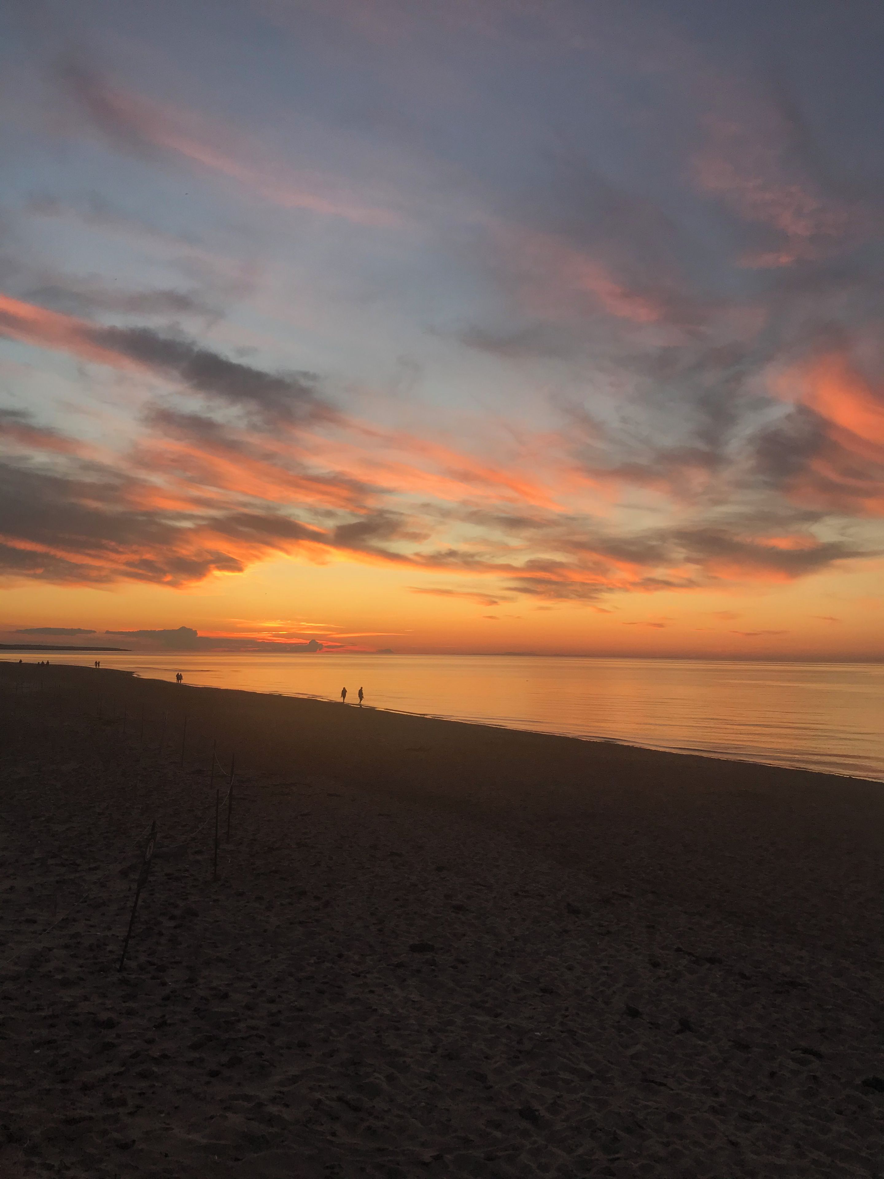 A beach with a sunset, calm sea, and distant horizon.