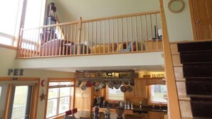A spacious kitchen with wooden cabinets, a dining area, and a loft bedroom with a balcony. - Cavendish Driftwood Getaway - Beach, National Park, Nature Trails, Seafood, Golf (Cavendish)