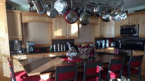 A modern kitchen with wooden cabinets, a central island with red chairs, and various kitchen appliances. - Cavendish Driftwood Getaway - Beach, National Park, Nature Trails, Seafood, Golf (Cavendish)