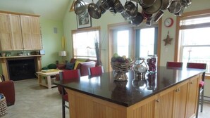 A kitchen with wooden cabinets, a central island, and a dining area with red chairs. - Cavendish Driftwood Getaway - Beach, National Park, Nature Trails, Seafood, Golf (Cavendish)