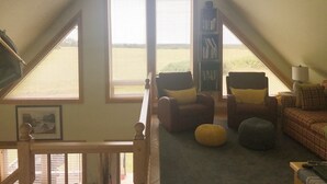 A cozy attic room with a large window, two armchairs, a bookshelf, and a view of the countryside. - Cavendish Driftwood Getaway - Beach, National Park, Nature Trails, Seafood, Golf (Cavendish)