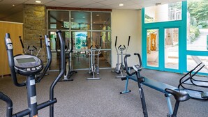 A gym with various exercise equipment, a stone wall, and large windows.
