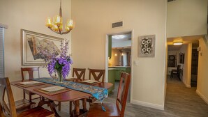 A dining area with a wooden table, chairs, and a chandelier. There is a vase with purple flowers on the table. - Entire house, pool, minutes to strip, Sleeps 10! Only 3 miles away from Strips (Las Vegas)