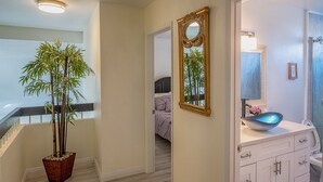 A hallway with a staircase, a potted bamboo plant, a bathroom with a large mirror, a sink with a blue bowl, and a bed in the background. - Entire house, pool, minutes to strip, Sleeps 10! Only 3 miles away from Strips (Las Vegas)