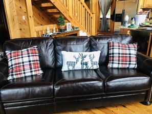 Eine dunkelbraune Ledersofa mit drei karierten Kissen und einem weißen Kopfkissen mit Hirschmotiven.